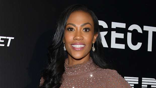 Kim Glass smiles for the camera wearing a light brown high-neck dress with silver sequins.